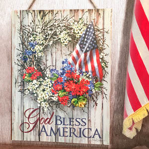 Featuring a beautifully crafted patriotic wreath adorned with vibrant red, white, and blue colored flowers and an American flag, this art piece is sure to capture the hearts of any proud American.  The powerful message of "God Bless America" is boldly written on the sign.