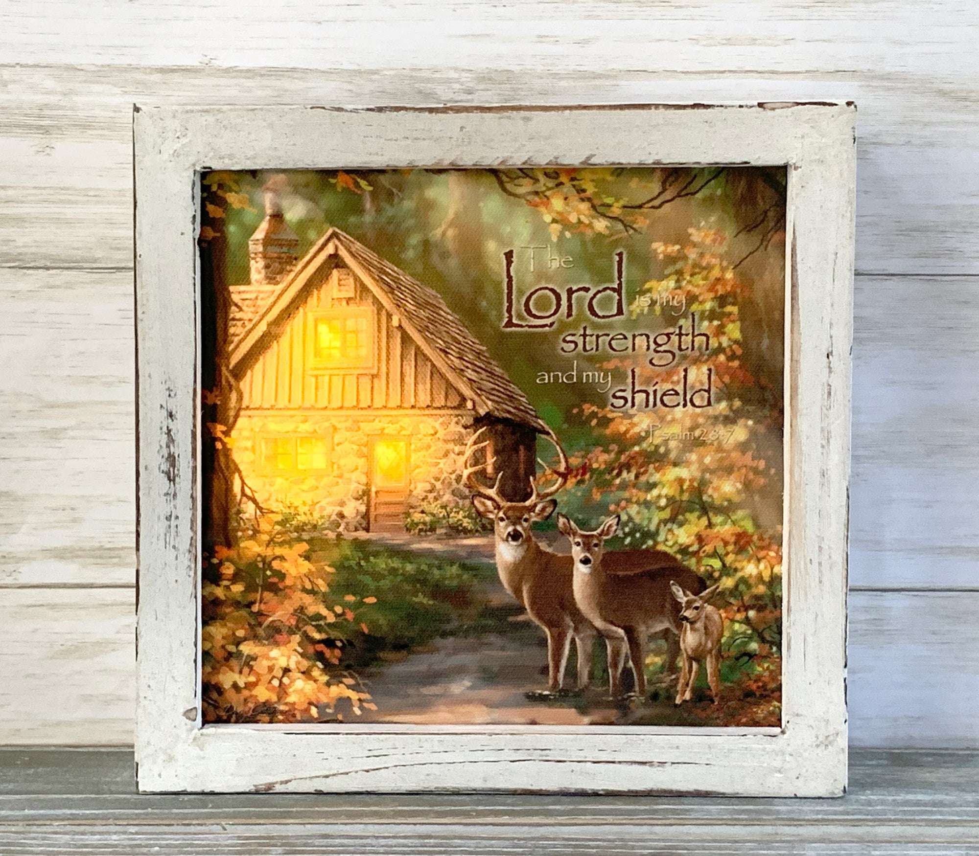 This exquisite piece features an old cottage standing proudly in the background, with a family of deer gracefully positioned in the foreground, surrounded by lush forests. The warm glow of the soft lighting creates a serene ambiance, perfect for unwinding after a long day.  This masterpiece also features the uplifting Psalm 28:7 scripture, "The Lord is my strength and my shield", written on the canvas.
