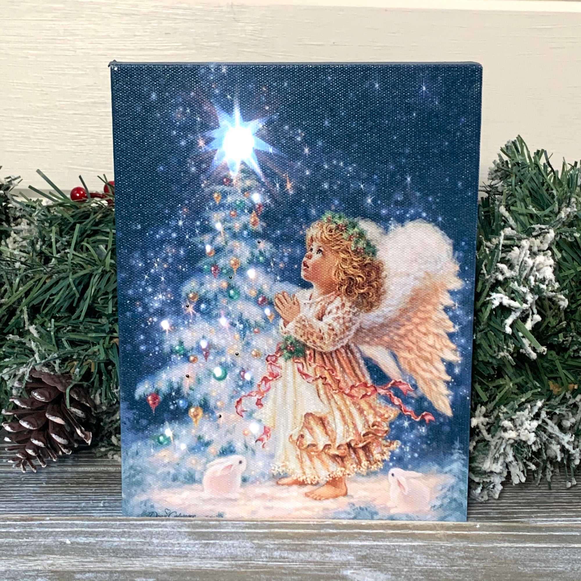 This enchanting piece captures the essence of winter wonderland with a young angel standing in front of a snow-covered and beautifully lit Christmas tree, adorned with sparkling ornaments and a shining star at the top.  As the snow falls gently around her, the angel's hands are pressed together in prayerful reverence, as if making a wish for all the blessings of the season.