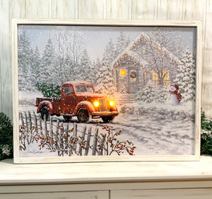 a charming vintage red truck parked in front of a cozy cottage.  Admire the details of the truck, with its fresh cut tree securely nestled in its bed, illuminated by the warm glow of its LED headlights. In the front yard of the cottage stands a jolly snowman, adding a touch of whimsy to the scene. And with lights strung up around the cottage.