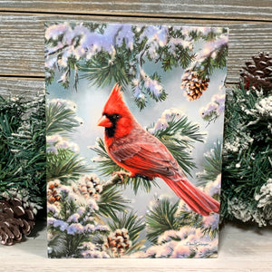 This beautiful canvas features a stunning red cardinal perched on a snow-covered branch, surrounded by delicate snowflakes and charming pinecones.