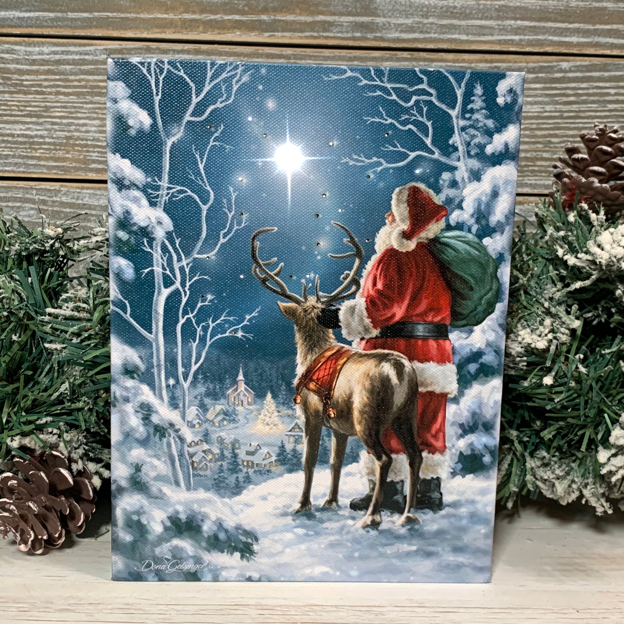 This enchanting canvas captures the essence of Christmas as Santa, dressed in his iconic red suit, holds his sack of presents alongside one of his trusty reindeer.  Beneath them lies a picturesque snow-covered town, eagerly awaiting the arrival of Santa and his gifts. And high above, a bright star shines down.