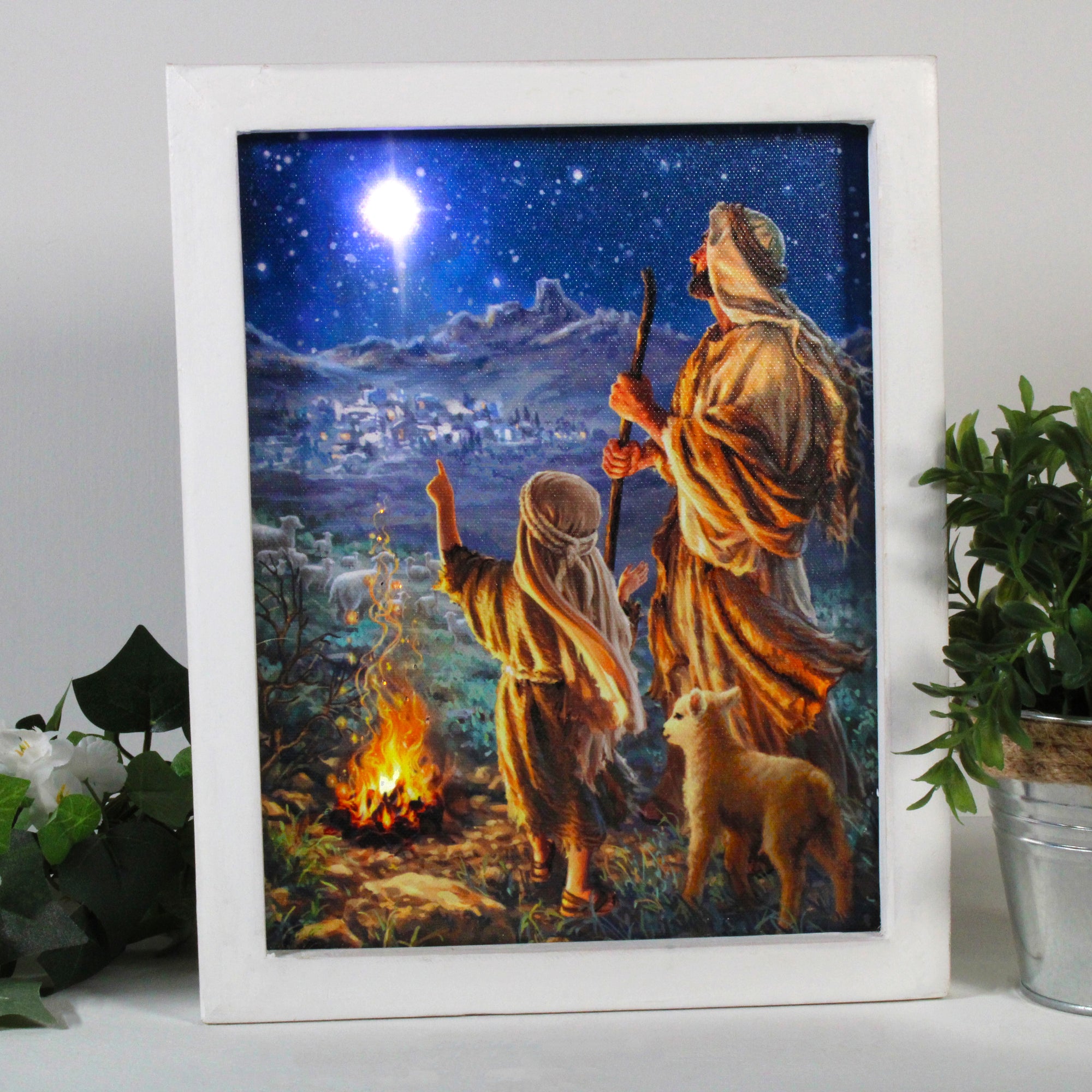 The scene before you depicts a tender moment shared between a shepherd and his son, as they stand by a cozy fire on a peaceful winter night. A gentle lamb stands between them, their faithful companion and a symbol of innocence and purity.  In the distance, you can see a small town nestled in the valley, bathed in a soft glow from the starry sky above. And there, high above the town, shines a single star, bright and radiant, a beacon of hope and guidance for all who seek it.
