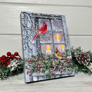  This exquisite piece captures the magic of the holidays with two adorable cardinals perched in front of a snow-covered window. One sits on a branch while the other rests on a garland, both gazing at the warm and inviting glow emanating from the candles on the other side of the window.  The flickering flames of the three candles bring a cozy and romantic ambiance to any room, making this canvas the perfect centerpiece for your holiday decor.