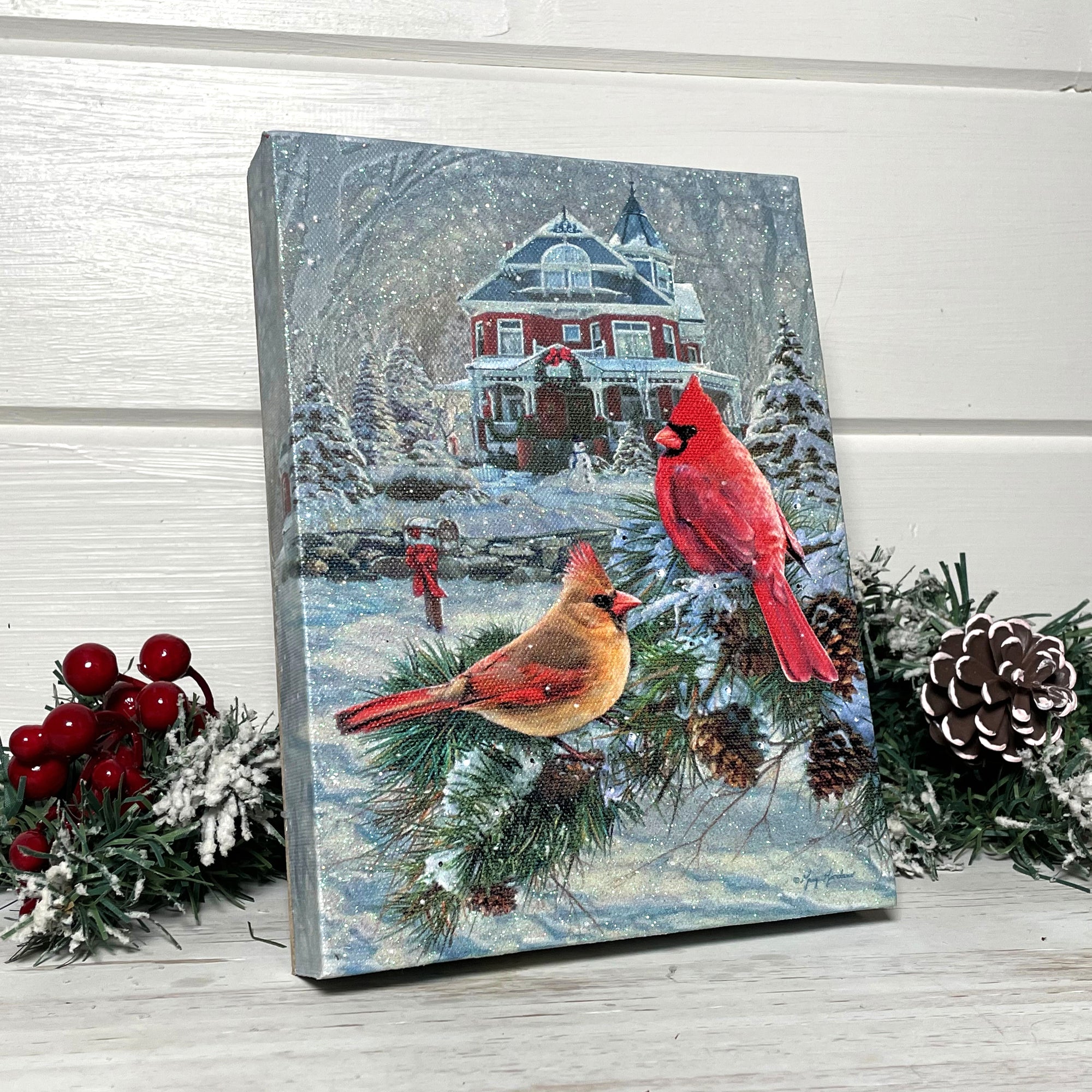  two cardinals sitting on a snow-covered branch and a charming Victorian house in the background. The wreath above the door and the snowman in the front yard add a touch of festive cheer to this picturesque scene.