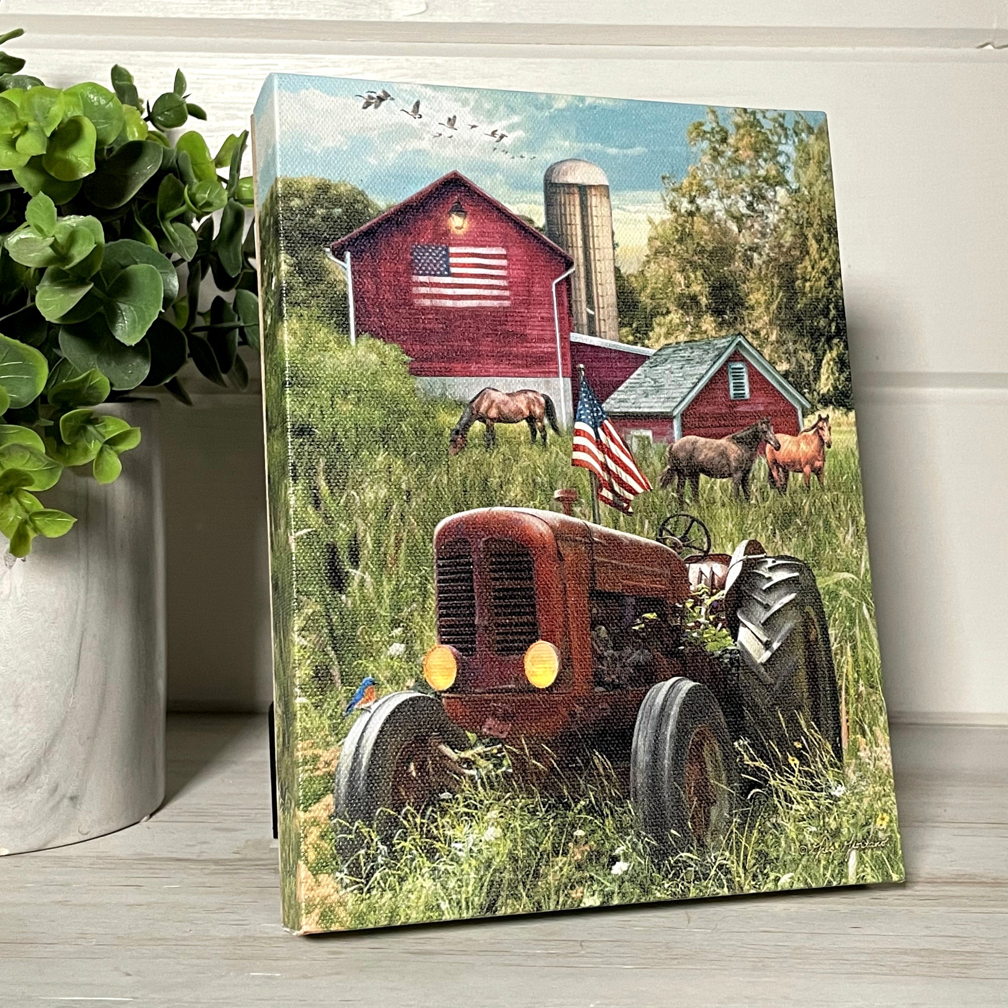  This stunning piece features a tractor standing tall in a picturesque field, proudly displaying the American flag. Behind the tractor stand three magnificent horses, a testament to the enduring spirit of the land.  As you take in the scene, your eye is drawn to the barn in the background, adorned with a grand American flag painted on its side.