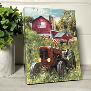  This stunning piece features a tractor standing tall in a picturesque field, proudly displaying the American flag. Behind the tractor stand three magnificent horses, a testament to the enduring spirit of the land.  As you take in the scene, your eye is drawn to the barn in the background, adorned with a grand American flag painted on its side.