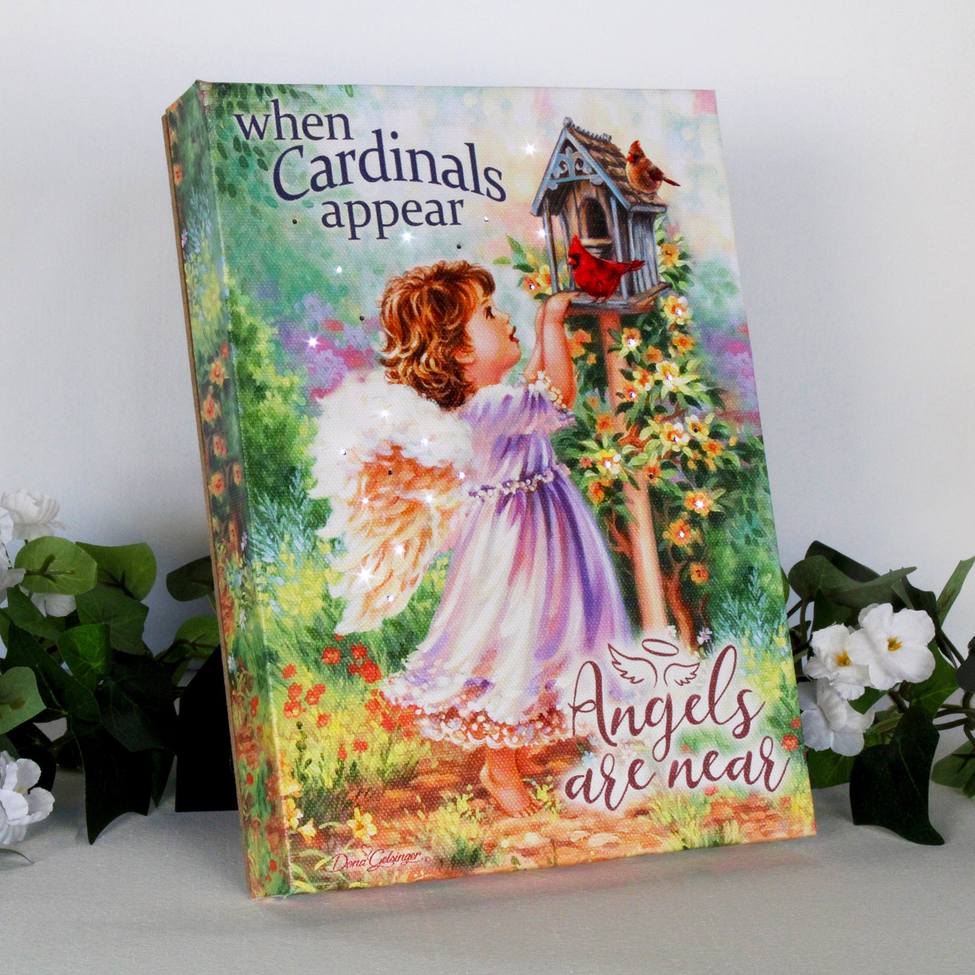 This captivating canvas features a young angel with shimmering wings, standing on her tippy toes to gaze upon two vibrant cardinals perched on a charming birdhouse. The forest scene is bursting with colorful blooms, creating a serene and inviting atmosphere.