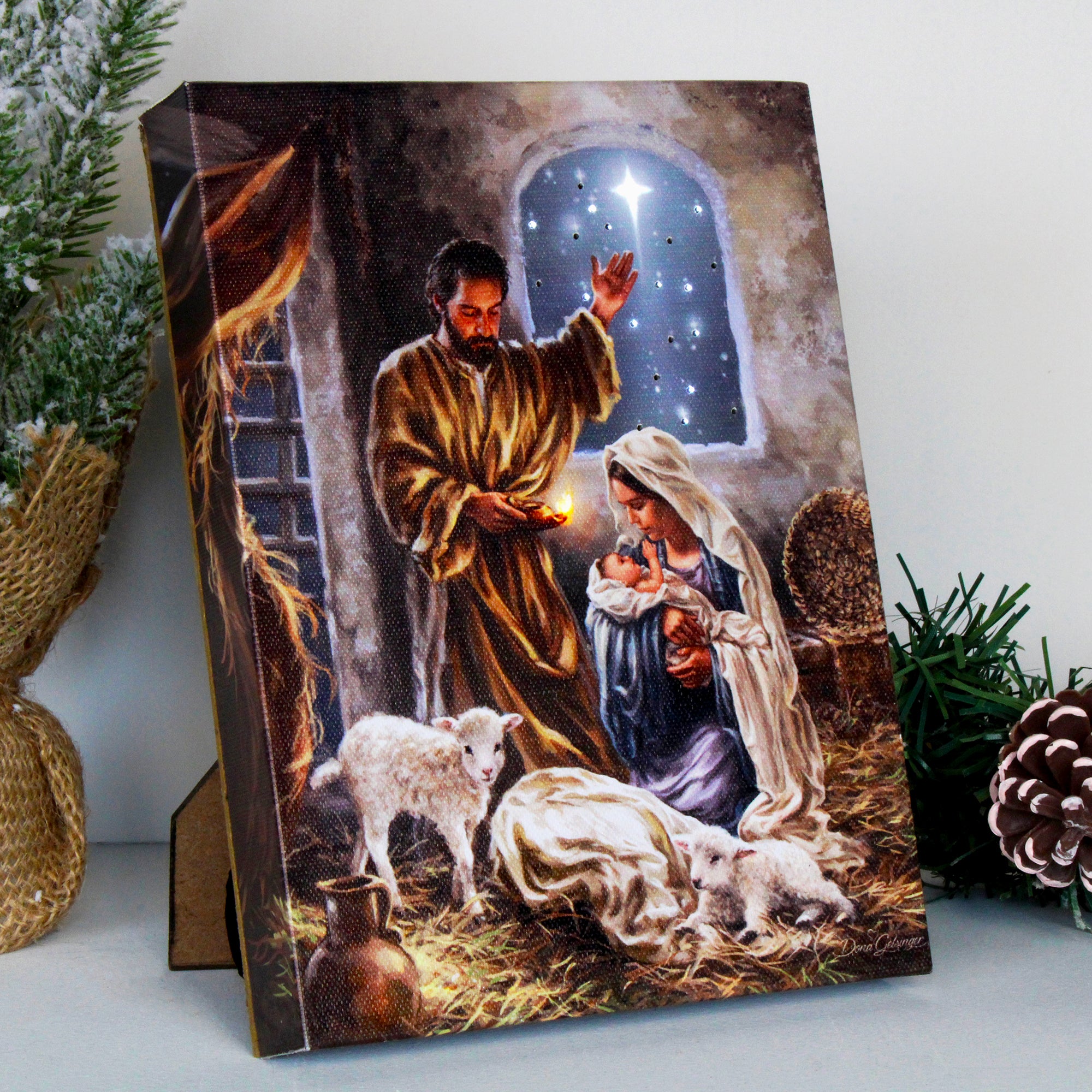 Jesus Christ. Mary kneels in awe, cradling her newborn baby, while Joseph stands by her side, illuminated by the soft glow of a candle. His outstretched hand points towards the star that led the way to this blessed event. Two gentle lambs rest nearby, adding to the peaceful scene.