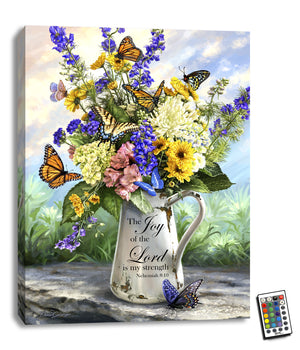 Featuring a charming tin watering can overflowing with a vibrant bouquet of flowers, this stunning piece is sure to brighten up any room. The message "The joy of the Lord is my strength" from Nehemiah 8:10 is written on the can in elegant script, reminding you of the power of faith and the beauty of nature.