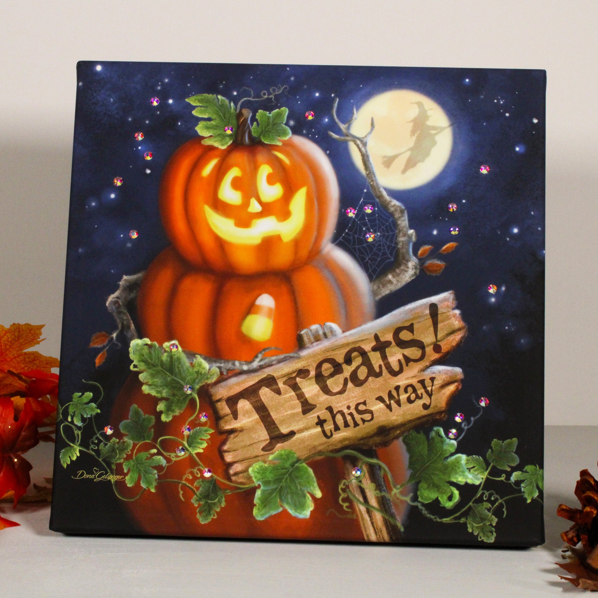 This delightful print features a whimsical jack-o-lantern perched on top of two plump pumpkins, creating a playful snowman-like figure that is sure to bring a smile to your face.  Guiding your way to the sweetest treats is a charming sign that reads "treats this way," adding a touch of magic to this already delightful scene. The backdrop of a full moon casts a romantic glow, while the silhouette of a witch flying on her broomstick across the moon.