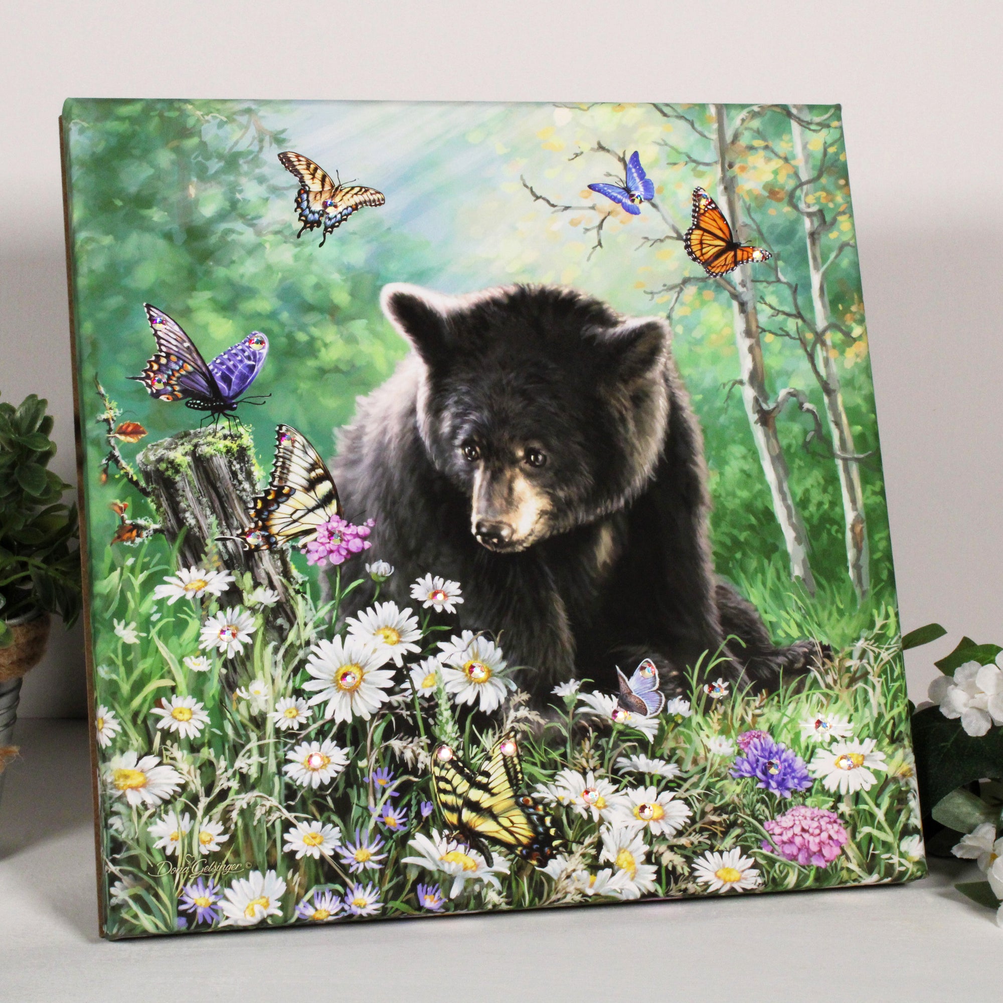  This breathtaking artwork features a majestic black bear, sitting serenely in a field surrounded by a myriad of colorful flowers and delicate butterflies, creating a picture of nature at its most magical.