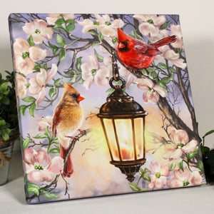 two adorable cardinals perched on a blooming tree, with a whimsical lantern chained to its trunk.  The delicate blossoms and lush foliage create an enchanting atmosphere