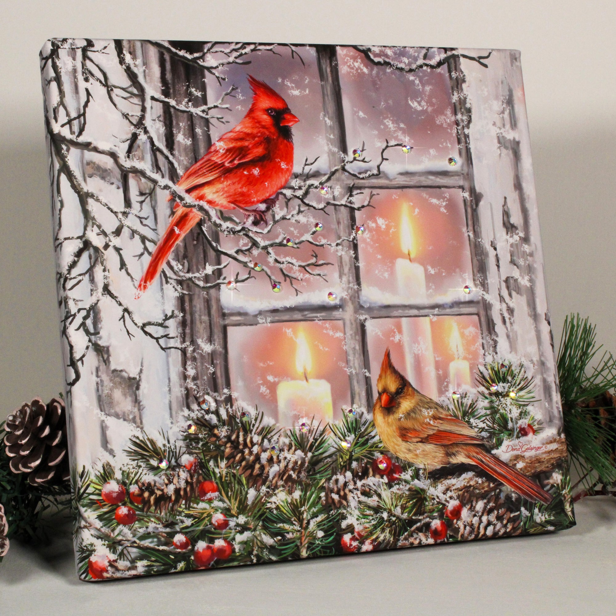 This enchanting work features two beautiful cardinals perched in a charming winter scene. One cardinal sits gracefully on a delicate branch, while the other perches atop a garland that adorns the window frame. The window itself is adorned with three lit candles.