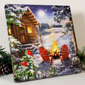 This picturesque scene captures the essence of the season with a cozy cabin nestled by a tranquil lake, two robins perched on a branch, and a warm fire crackling in two Adirondack chairs.