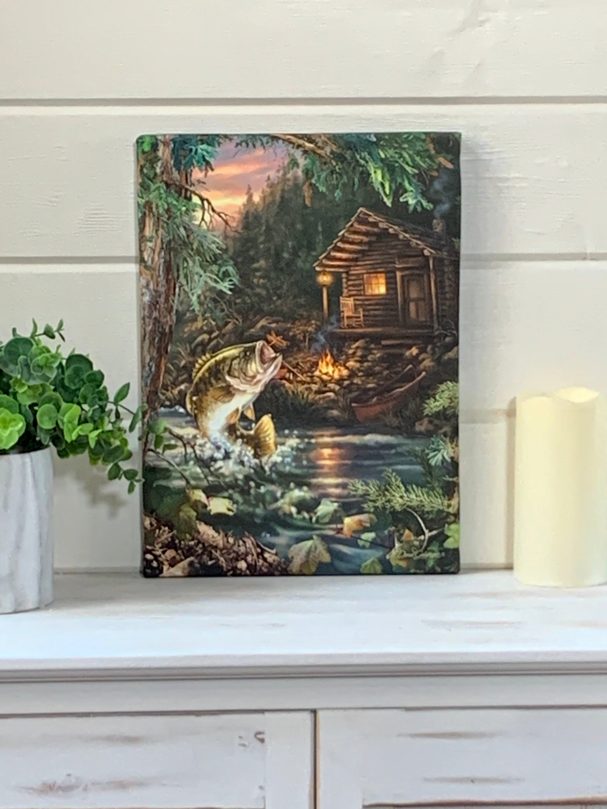 This piece captures the essence of a peaceful lakeside retreat, where a lone fish leaps out of the water with eager anticipation to catch a dragonfly hovering above the shimmering surface.  Take a closer look and you'll spot a cozy cabin nestled just off the bank, inviting you to imagine the warm glow of a fire flickering outside on a cool evening. And what's that by the shore? It's a canoe, waiting for your next adventure on the water.
