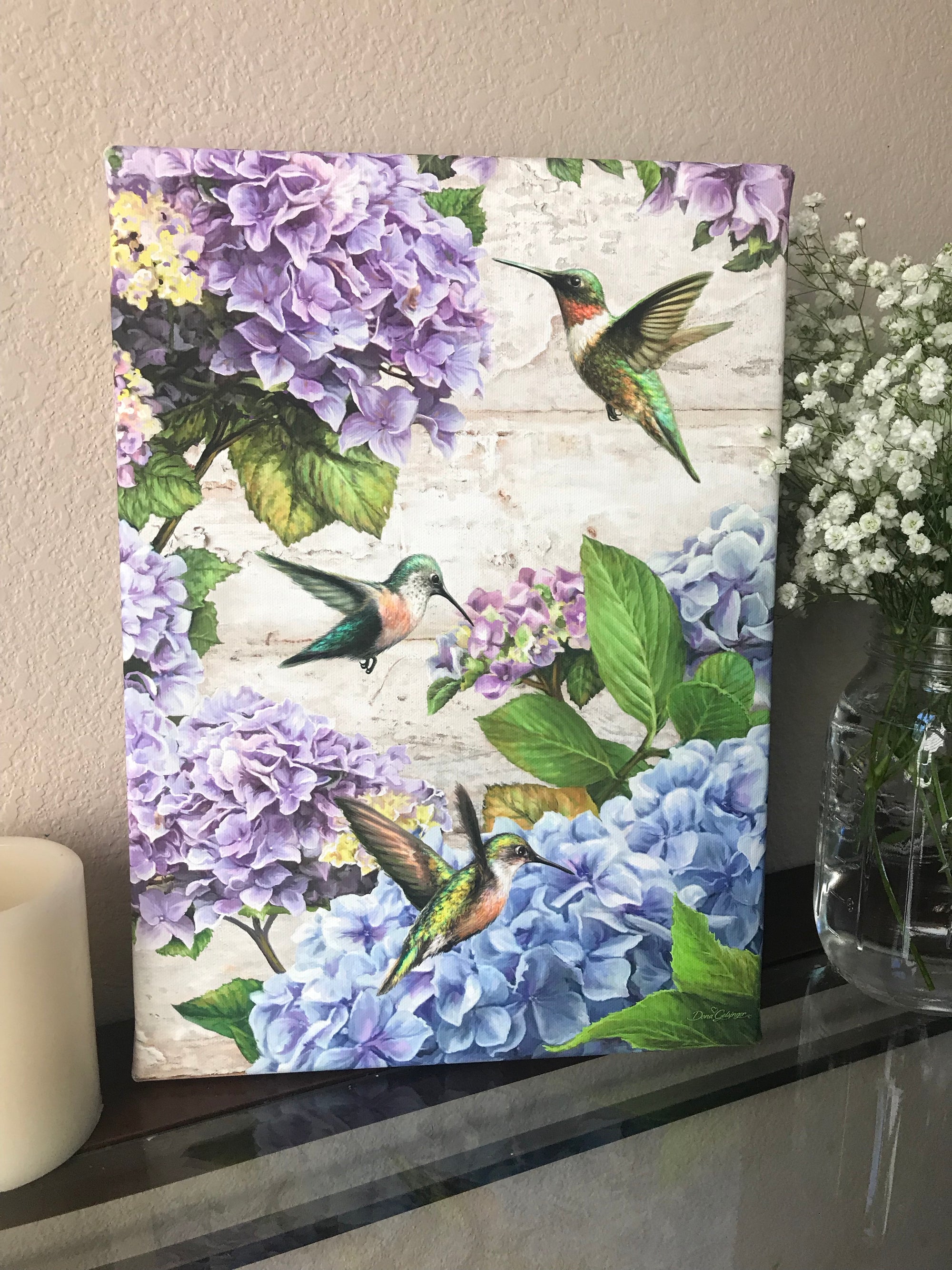 Indulge in the beauty of nature's most enchanting creatures with our Hummingbirds and Hydrangeas Canvas Wall Art. This stunning piece showcases vibrant purple and blue hydrangeas that serve as a delectable feast for the delightful hummingbirds.  The intricate details of the hummingbirds' wings and feathers are captured in breathtaking clarity.