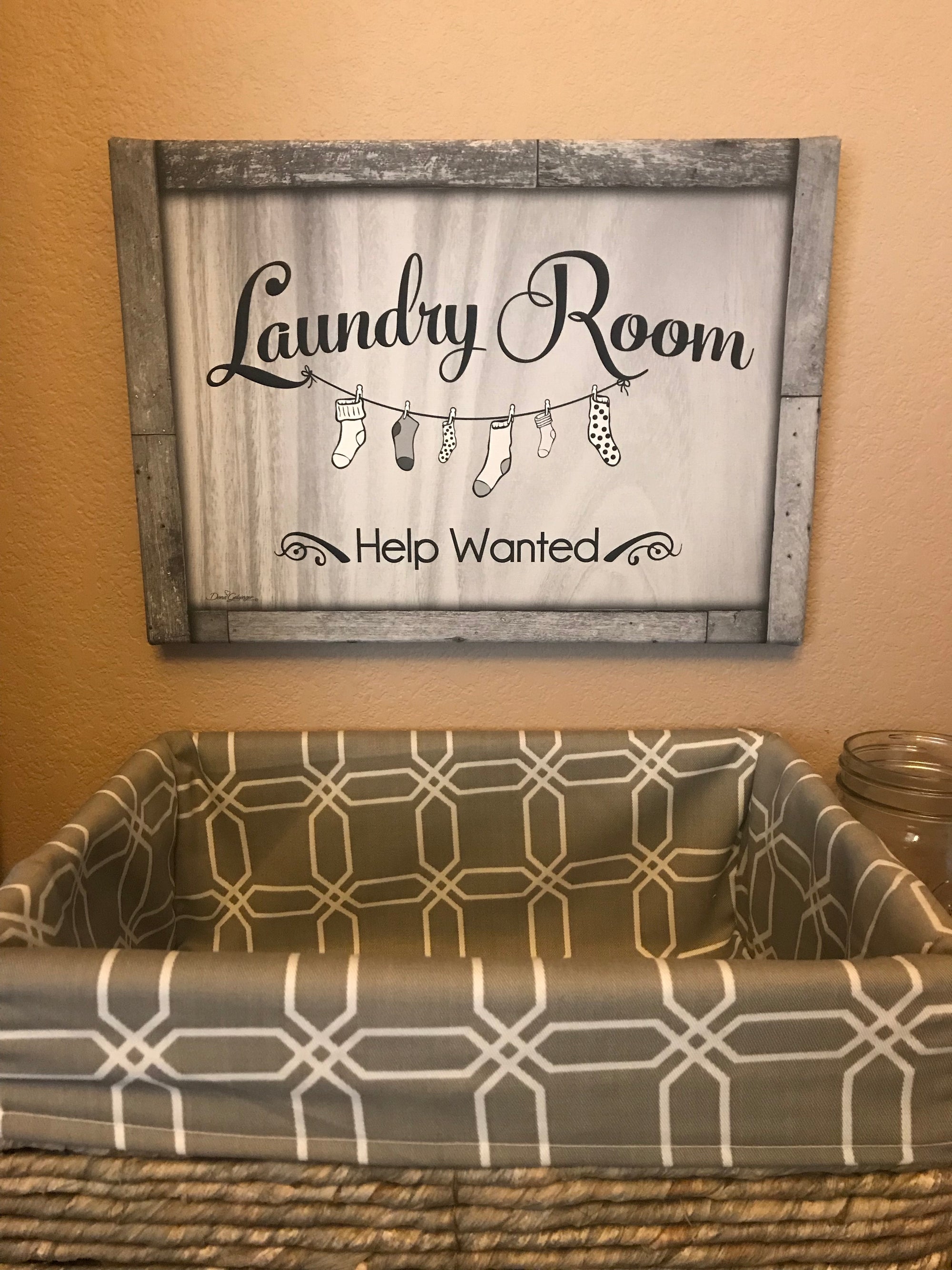 Featuring a playful design of a laundry line with socks pinned to it, the L and R are cleverly connected to the line, adding a touch of whimsy to the piece.  Hang this canvas on your laundry room wall and let the fun and romantic vibe flow in! The text "Laundry Room Help Wanted" is written in a beautiful font.