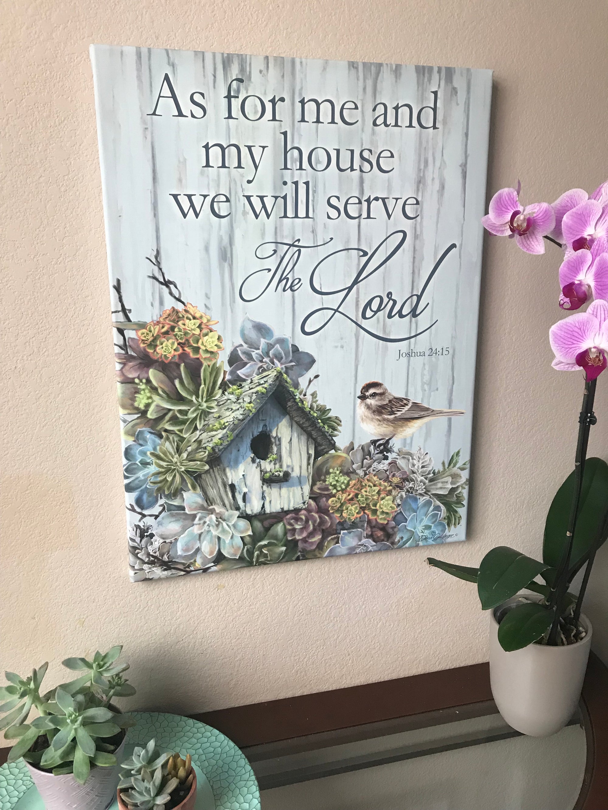  This exquisite piece features a charming birdhouse nestled amongst lush succulent plants, with a sweet little bird perched atop one of the succulents, adding a touch of whimsy to the scene.  The canvas is adorned with the timeless words of Joshua 24:15, "As for me and my house we will serve the Lord,"