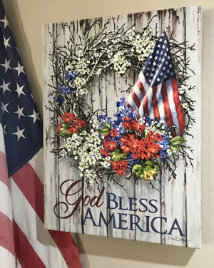 Adorned with a beautiful wreath made of vibrant red, white, and blue flowers, this piece is sure to add a touch of Americana to any space. And with the American flag proudly displayed at its center, you'll feel a sense of patriotism every time you gaze upon it.  The canvas itself features the heartfelt message "God Bless America."