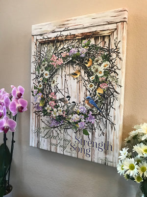Adorned with a gorgeous wreath bursting with vibrant multicolored flowers and an array of delightful birds, this piece is sure to bring a touch of nature's wonder to any room.  Emblazoned with the inspiring words of Exodus 15:2, "The Lord is my strength and my song."