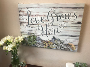 The elegant cursive writing on the canvas beautifully spells out the heartwarming message, "love grows here," a simple yet profound reminder of the love that blossoms in your home.  The unique touch of the heart-shaped "e" in the word "here" adds a touch of romance