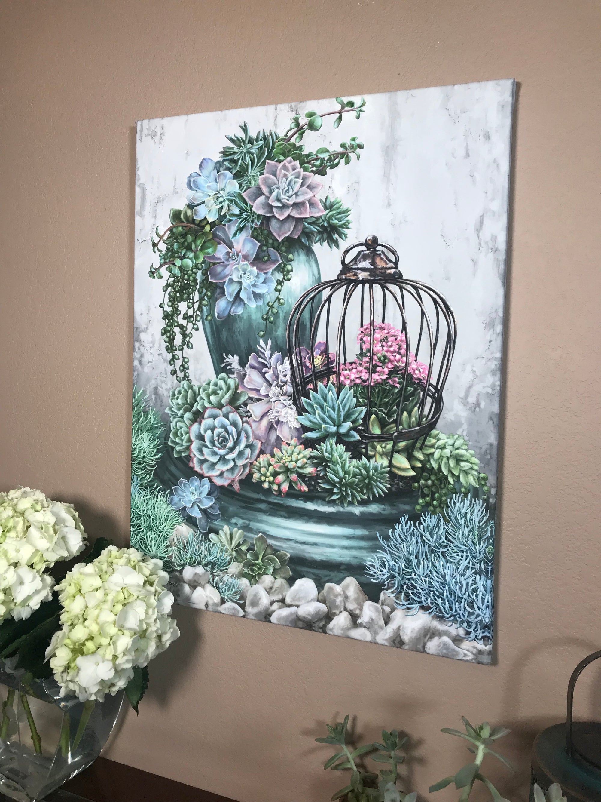 The delicate greenery and vibrant hues of the succulents are brought to life in stunning detail, capturing the essence of nature's beauty.  Set against a backdrop of textured canvas, an array of succulents takes center stage. Some nestled in a charming birdcage, while others flourish in a potted paradise.